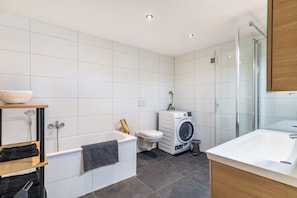 A modern bathroom with a bathtub, a washing machine, a toilet, and a glass shower enclosure. - Apartment 'Winder' with Mountain View, Private Terrace and Wi-Fi (Lustenau)