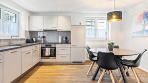 Et moderne køkken med hvide skabe, et spiseområde med et rundt bord og sorte stole, samt en hængende lampe.
