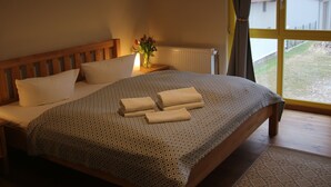 A bedroom with a large bed, wooden headboard, and a window with curtains. - Bäumi-Hof  (Oberuckersee)