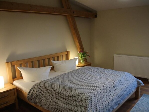 Ein Schlafzimmer mit einem Holz-Kopfteil, einem Bett mit gemustertem Überwurf, einem Nachttisch mit Lampe und einem Blumentopf.