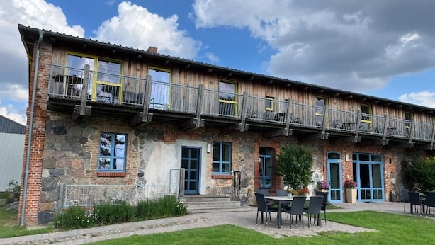 A rustic building with a balcony, outdoor seating, and a stone facade. - Bäumi-Hof  (Oberuckersee)