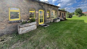 A brick building with yellow-framed windows and a wooden bench in the yard. - Bäumi-Hof  (Oberuckersee)