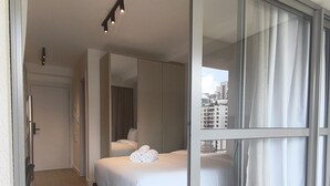 Una camera d'hotel moderna con un'ampia porta scorrevole in vetro, un letto con lenzuola bianche e vista sulla città.