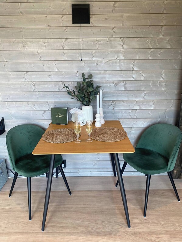 A wooden table with two green chairs, a vase with greenery, and two candles. - Black Mirror , Jacuzzi all Year (Asker)
