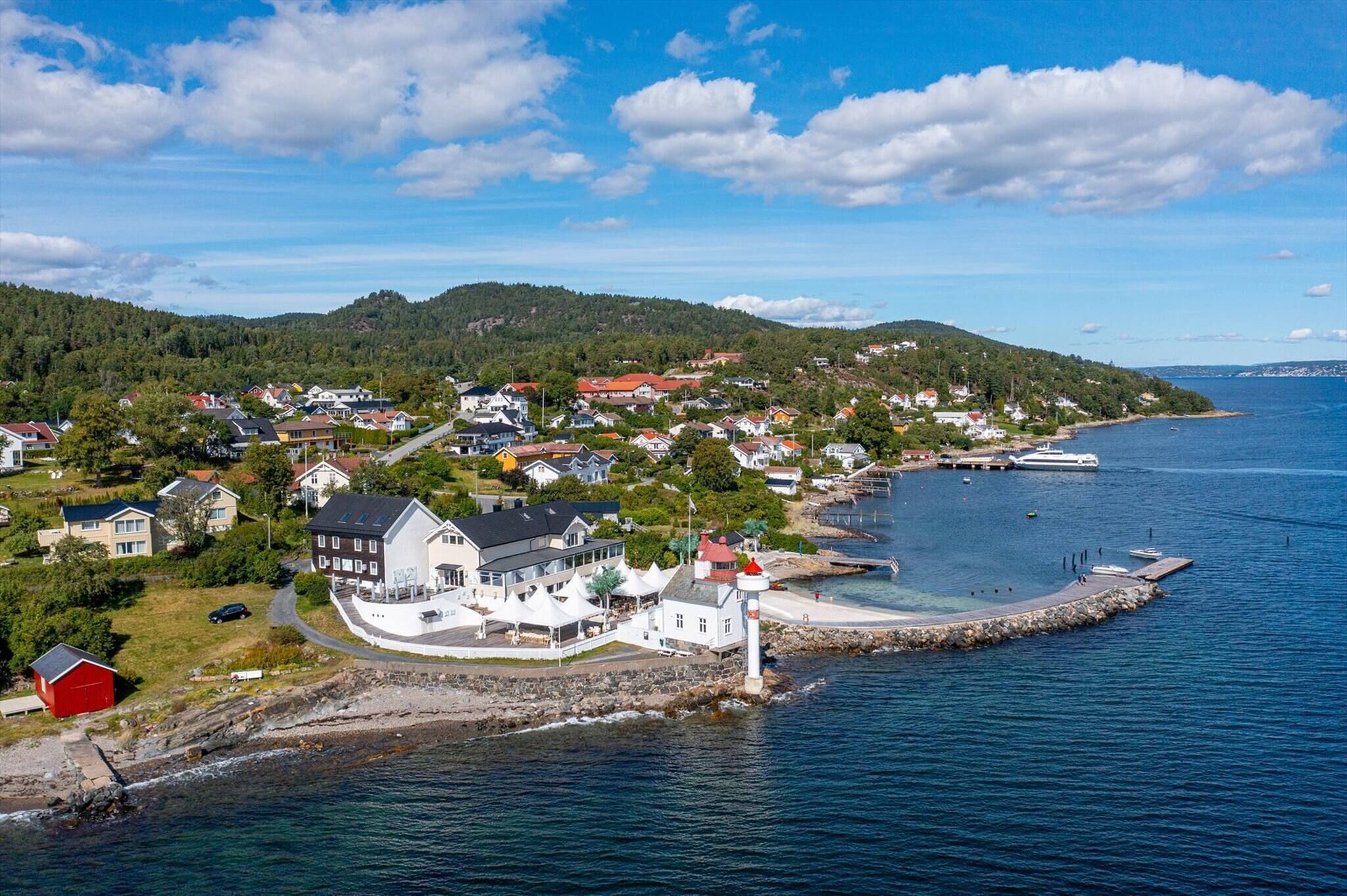 A coastal town with a prominent white building near the water, a lighthouse, and a rocky shoreline.