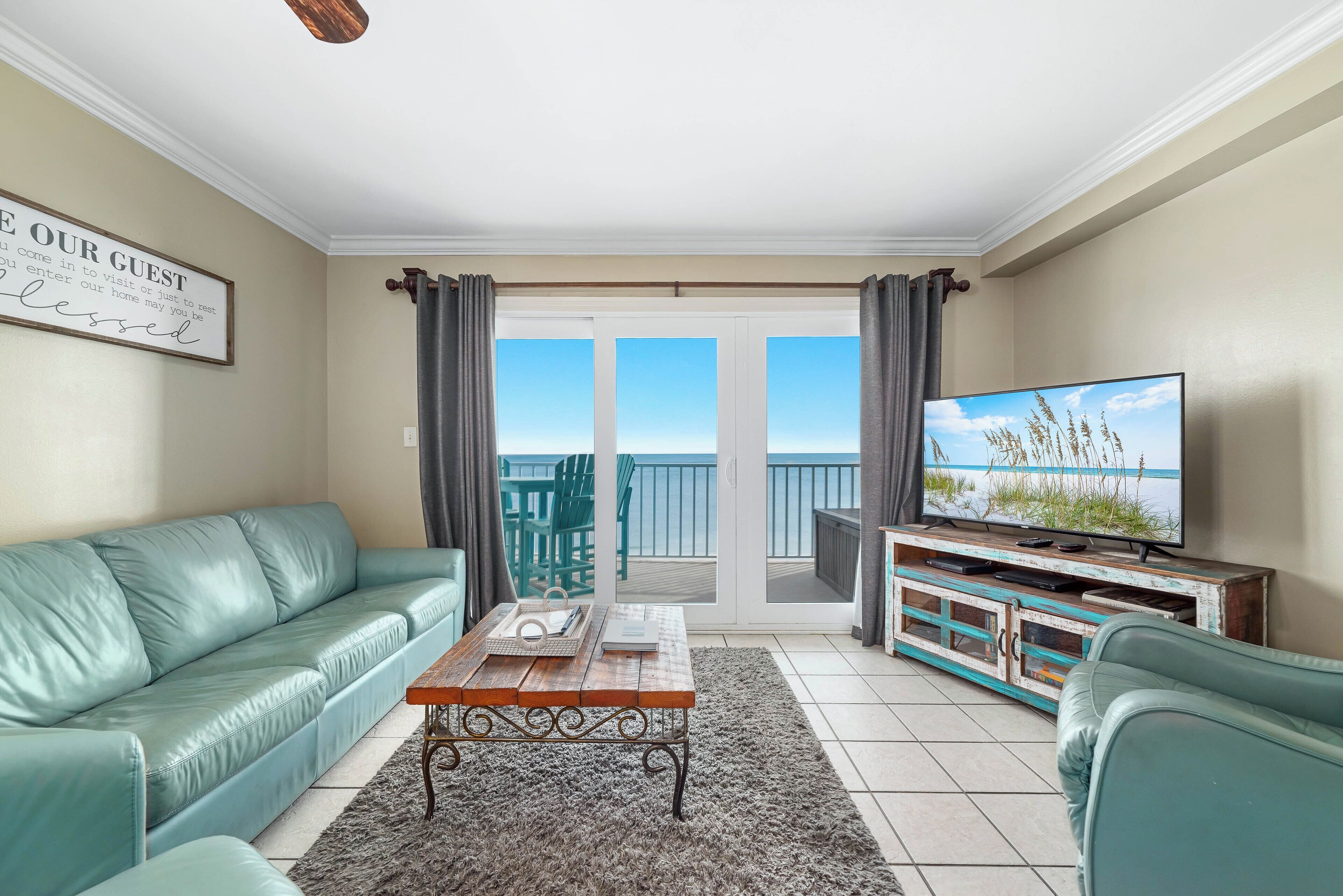 A living room with a green sofa, a wooden coffee table, a television on a wooden stand, and a view of the balcony.