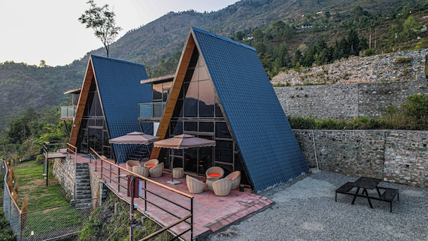 A modern building with two triangular roofs, outdoor seating, and a stone wall. - Alaya Stays Echo By The Lakes (Bhimtal)
