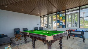 A pool table in a room with large windows, a sofa, and a foosball table. - Alaya Stays Echo By The Lakes (Bhimtal)