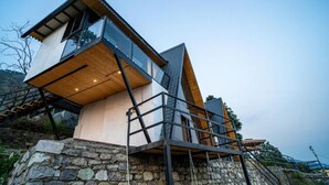 A modern house with a stone base, large windows, and a wooden upper structure. - Alaya Stays Echo By The Lakes (Bhimtal)