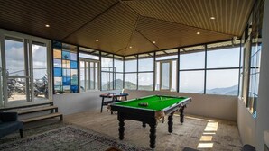 A spacious room with a pool table, a sofa, and large windows offering a mountain view. - Alaya Stays Echo By The Lakes (Bhimtal)