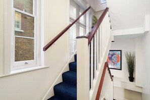 Una escalera con barandilla de madera, un rellano con alfombra azul y una obra de arte enmarcada en la pared.