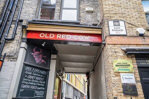 A narrow alleyway with a pub named 'Old Red Cow' on the left, a sign for 'East Passage EC1' above, and a 'Deep Tissue Massage' sign on the right. - Cozy Studio in the Heart of the City of London A (London)