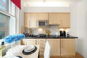 Una cocina moderna con armarios de madera, un microondas integrado y un comedor con una mesa lista para dos personas.