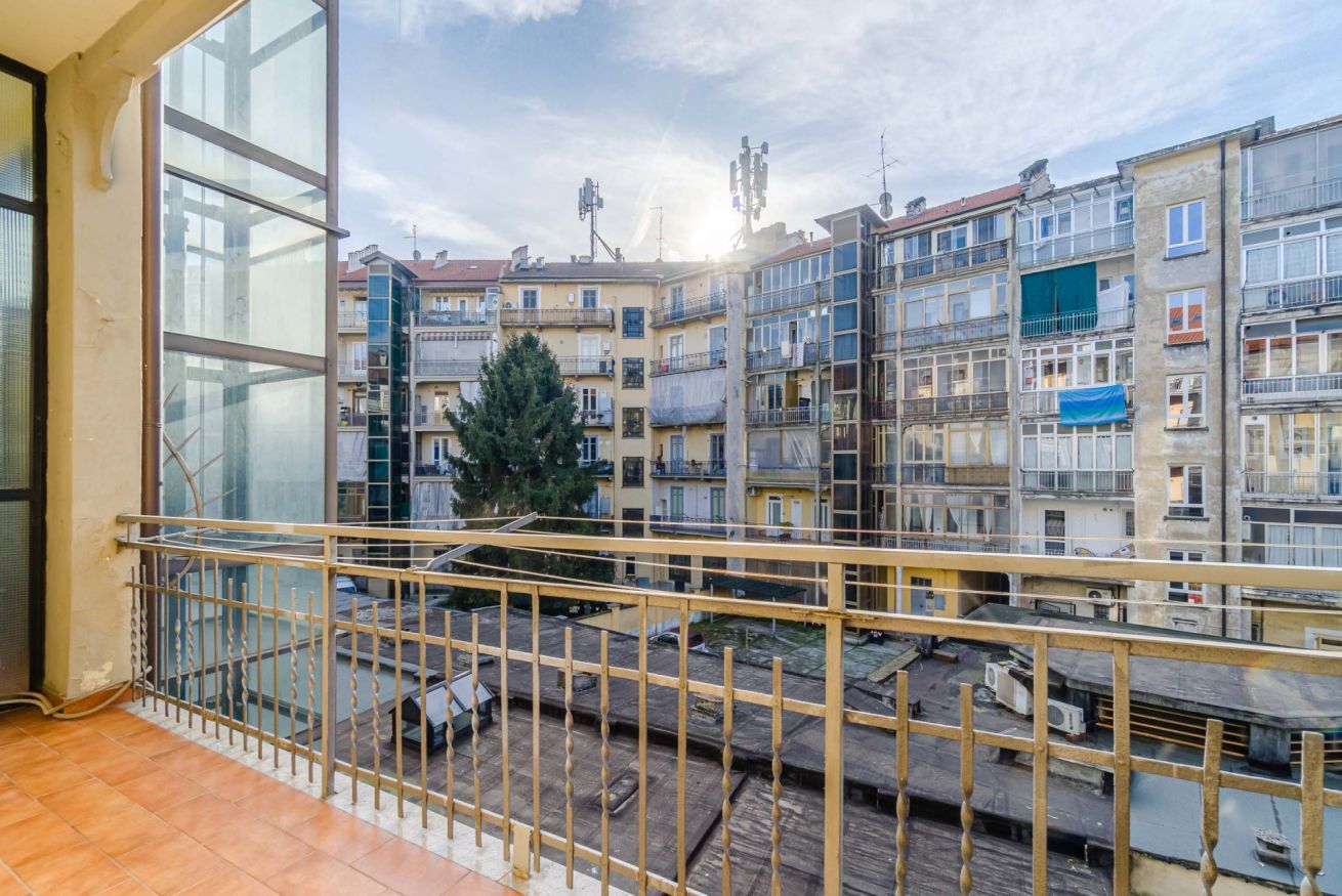 Ein Balkon mit Metallgeländer, der auf ein Wohngebiet mit mehrstöckigen Gebäuden blickt.