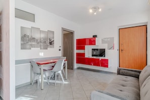 Un soggiorno moderno con zona pranzo, un divano e una TV su un mobile rosso e bianco.