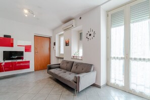 A modern living room with a sofa, a TV, and a red kitchen unit.