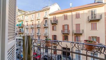 Ein Balkon mit schmiedeeisernen Geländern, Terrakottatöpfen und Blick auf mehrstöckige Gebäude mit Balkonen und Fensterläden.