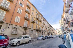 A street lined with multi-story buildings, parked cars, and a clear sky.