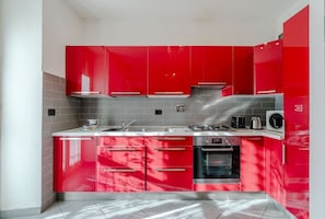 A modern kitchen with red cabinets, stainless steel appliances, and a tiled backsplash.