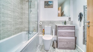 A modern bathroom with a glass shower enclosure, a toilet, a sink with a mirror, and a wooden vanity. - City View Apartment Near Manchester City Centre (Salford)