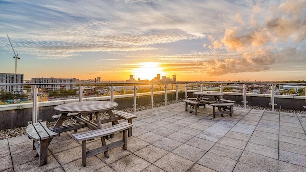 A rooftop terrace with picnic tables and a view of the sunset over a city skyline. - City View Apartment Near Manchester City Centre (Salford)