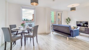 A modern living room with a round dining table, grey chairs, a blue sofa, and a TV. - City View Apartment Near Manchester City Centre (Salford)