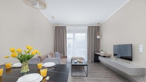 Una sala de estar moderna con una mesa de comedor para dos personas, un sofá, una mesa de centro y un televisor montado en la pared.