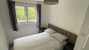 Ein Schlafzimmer mit einem Bett, einem Nachttisch, einem Fenster mit Vorhängen und einer Pendelleuchte.