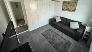 Ein modernes Wohnzimmer mit einem grauen Sofa, einem kleinen Beistelltisch, einem grauen Teppich und einem weißen Kleiderschrank mit Spiegel.
