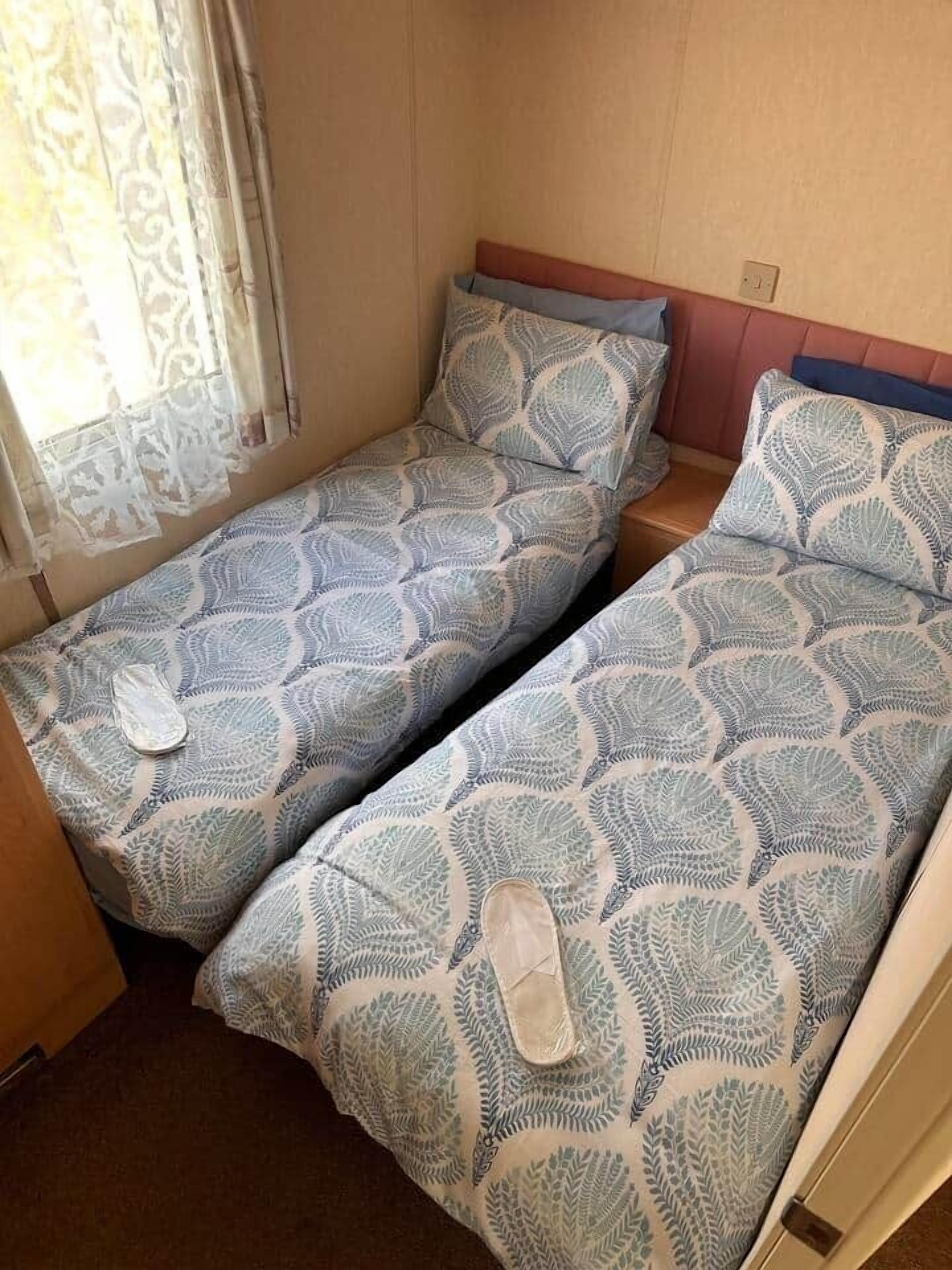 Een kleine kamer met twee eenpersoonsbedden, elk met een beddekleed met patroon en een kussen.