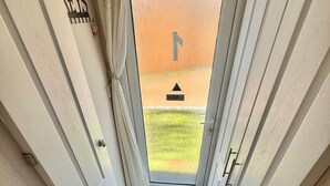 Ein schmaler Flur mit einer Tür zu einem Außenbereich, einer schwarzen Matte vor der Tür und einem Schild an der Wand.