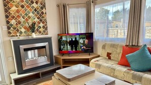 A modern living room with a fireplace, a television, and a sofa with cushions. - Deluxe Delta 4-bedroom Caravan (Uddingston)