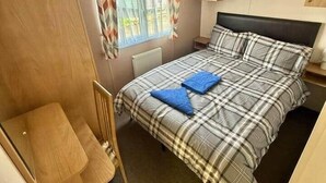 A compact bedroom with a bed, a small desk, and a window with curtains. - Deluxe Delta 4-bedroom Caravan (Uddingston)