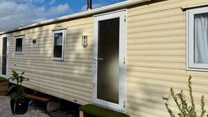 A mobile home with a sliding door, a small window, and a chimney. - Deluxe Delta 4-bedroom Caravan (Uddingston)
