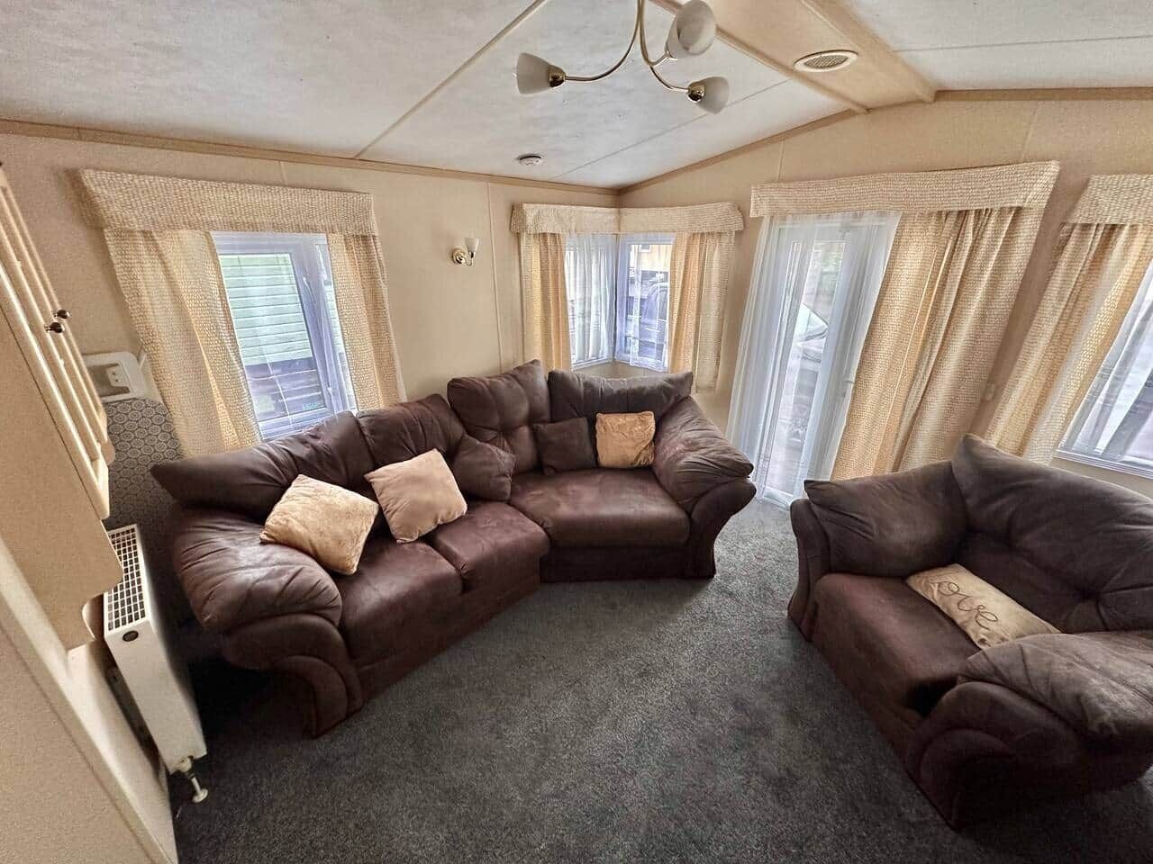 A room with a large L-shaped brown leather sofa, two beige cushions, and a small brown armchair.