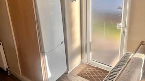 Une petite cuisine équipée d’un réfrigérateur, d’un placard étiqueté « CLÉS » et d’une porte marquée « PRODUITS DE NETTOYAGE ».