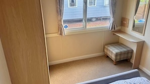 Une chambre avec une fenêtre, une armoire en bois, un petit banc et un miroir au mur.