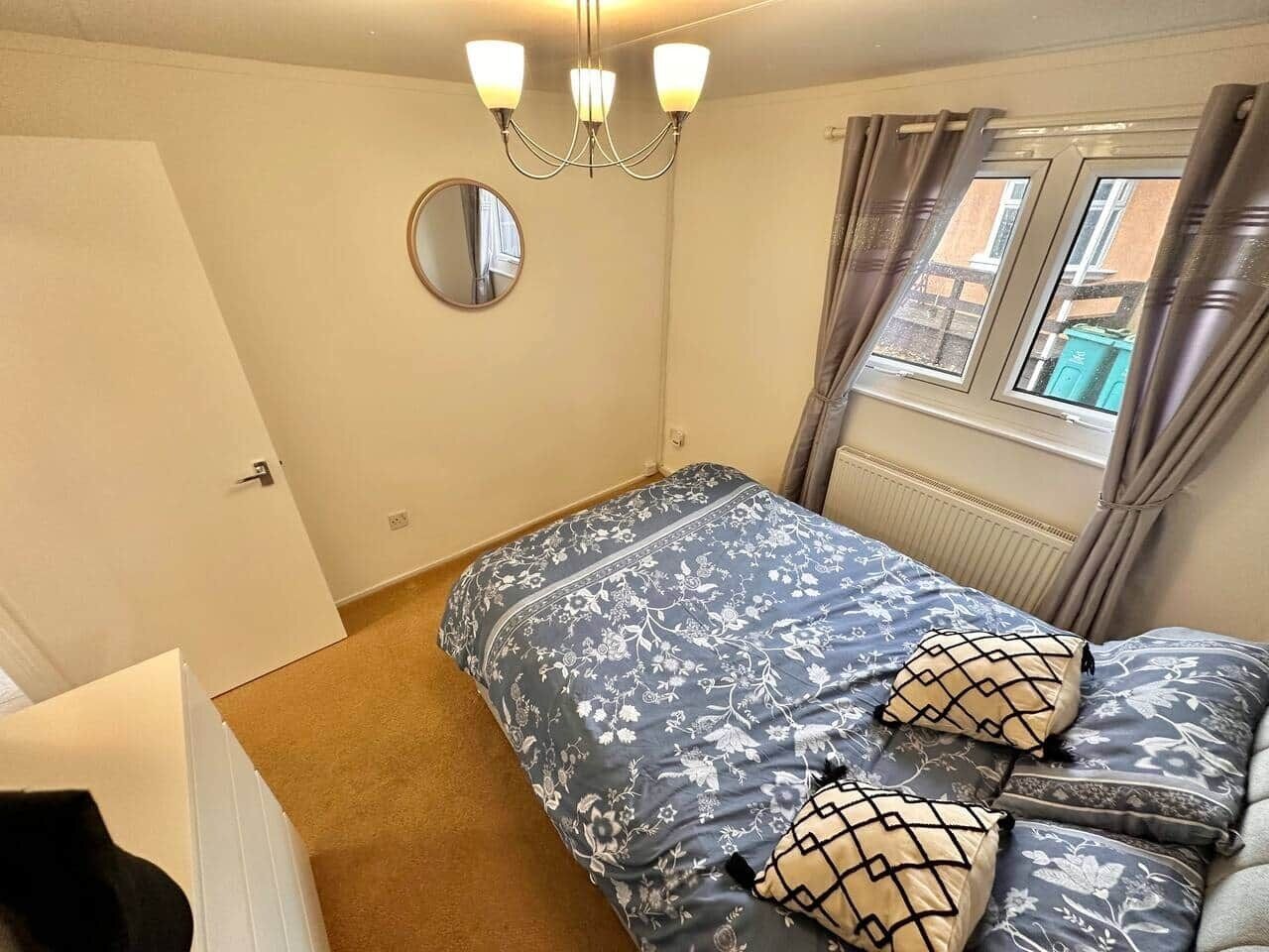 Et soveværelse med seng, lysekrone, et vindue med gardiner og en radiator.