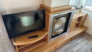 Un espacio habitable compacto con un televisor de pantalla plana sobre un soporte de madera, un horno empotrado y una pequeña cocina.