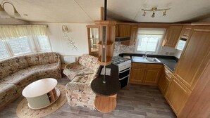 Interior compacto de una caravana con zona de estar, kitchenette y una hornilla colgante.