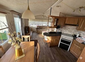 A compact kitchen with wooden cabinets, a stove, and a dining area with a table and chairs. - Willerby Granada 2 Bed Caravan Uddingston Glasgow (Uddingston)