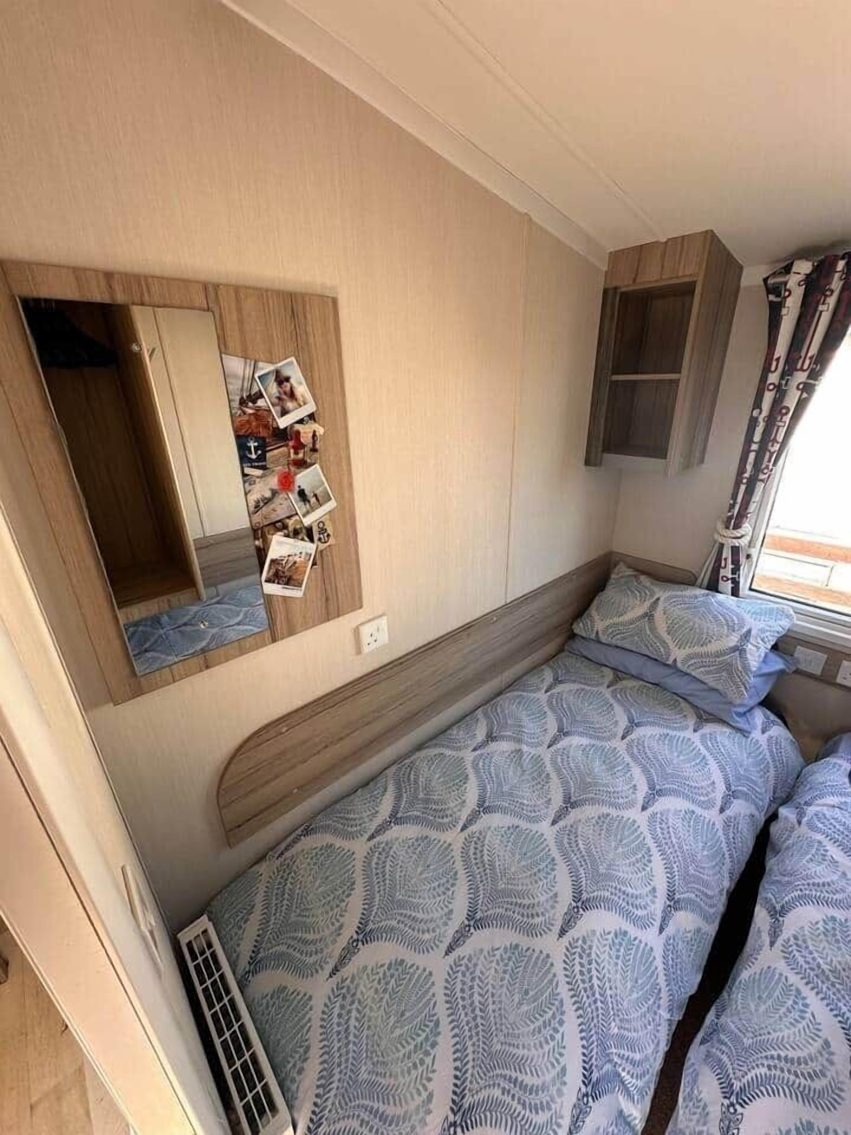A compact RV bedroom with a bunk bed, a small cabinet, and a mirror with photos.