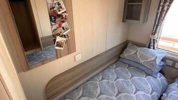 A compact RV bedroom with a bunk bed, a small cabinet, and a mirror with photos.