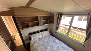 Un dormitori modest amb llit, prestatges integrats, una finestra amb cortines i vista a l'exterior.