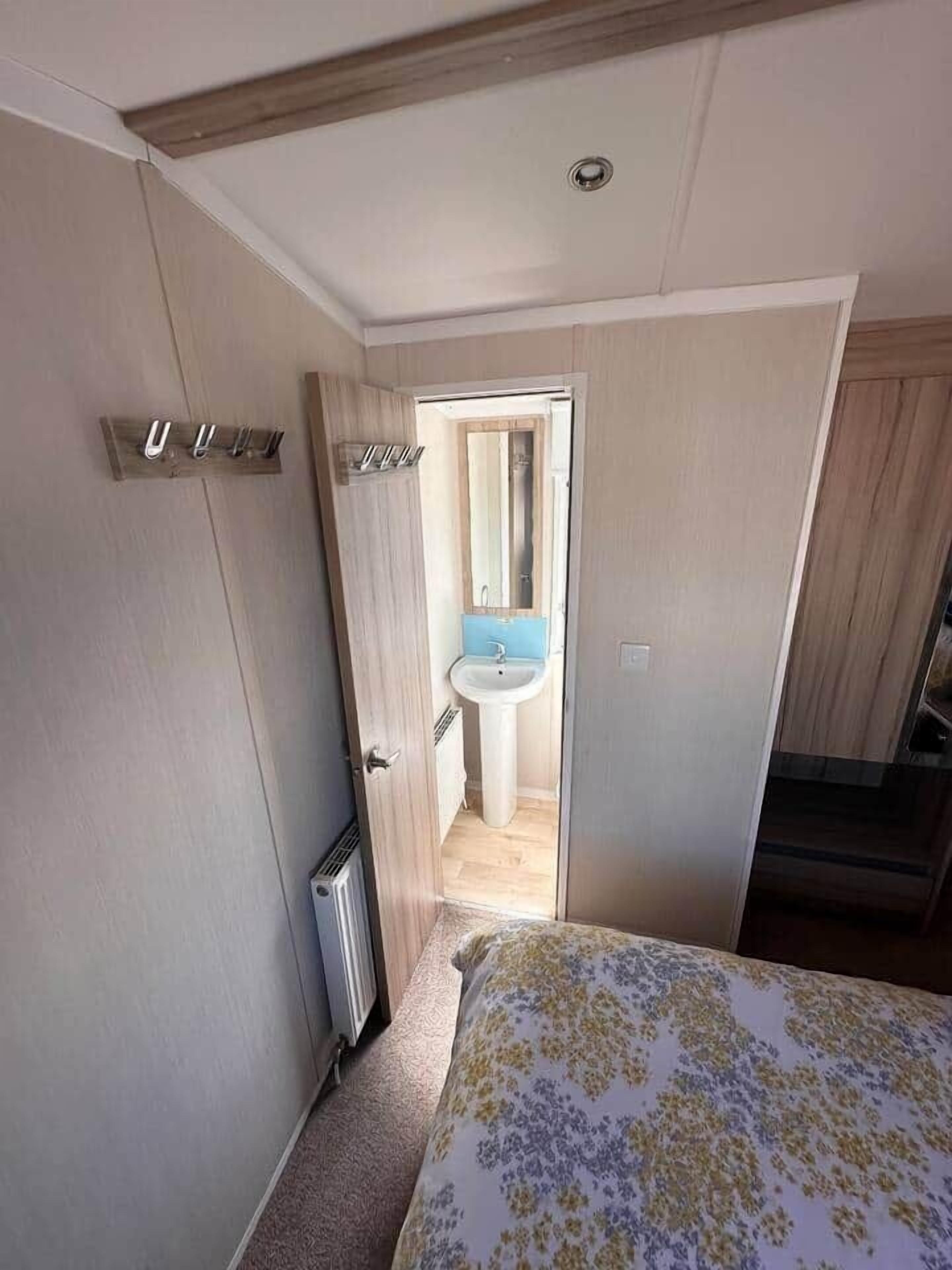 Une chambre à coucher comprenant un lit, un radiateur, une porte donnant sur une salle de bain avec un lavabo, et un plafond en bois.