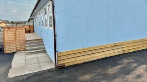 A single-story building with a blue exterior, a wooden deck, and a set of steps leading to a door.