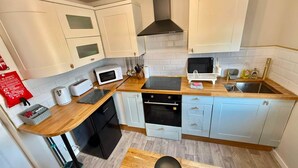 A compact kitchen with white cabinets, a black range hood, a microwave, a toaster, and a sink.