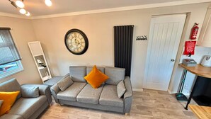 A living room with a grey sofa, a wall clock, a bookshelf, and a door labeled 'KEYS'.