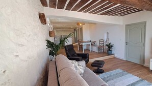 Una sala de estar con un sofá, sillas, un televisor y una zona de comedor al fondo.