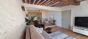 A living room with a sofa, chairs, a TV, and a dining area in the background. - Apartment in the heart of the medieval village with a view of the sea   (Tourrettes-sur-Loup)